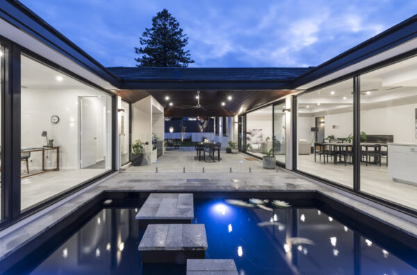 Lap pool lit at night between glazed living pavilions