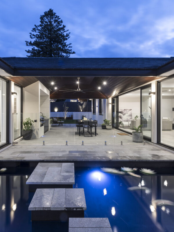 Lap pool lit at night between glazed living pavilions