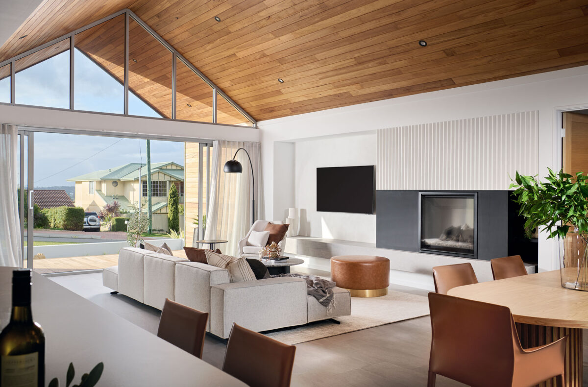 Modern, light filled living area with raked ceilings, full glass wall, wooden ceiling anda a fireplace
