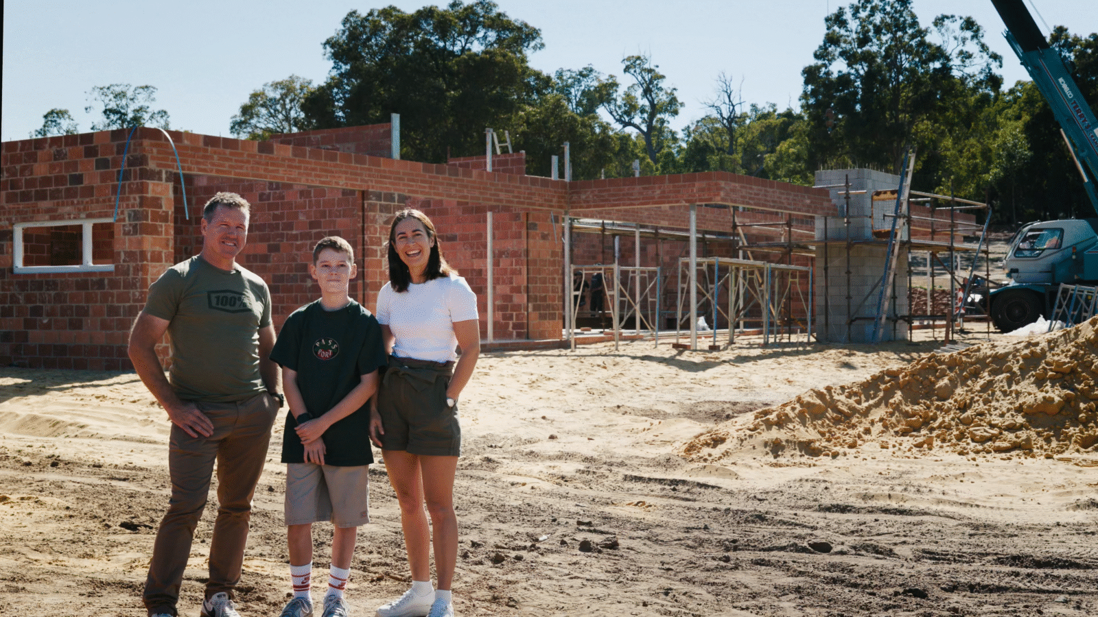 Oswald Homes custom home clients Glenn, Amy and Kingston stand proudly in front of their in-construction, custom-built home sitting among the backdrop of glorious bush views in Perth southern suburbs.