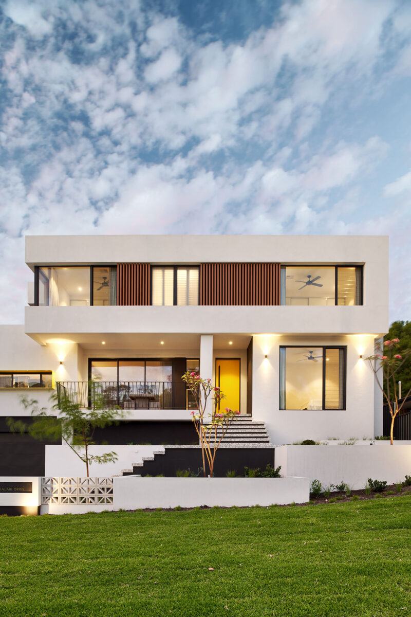 Two storey home at dusk with white render and timber upper level