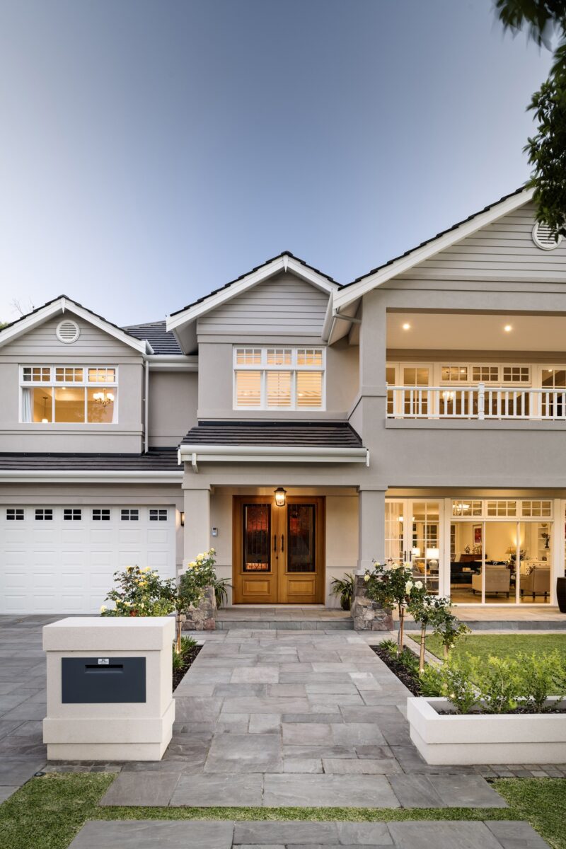 Two storey Hamptons style home at dusk with lit windows
