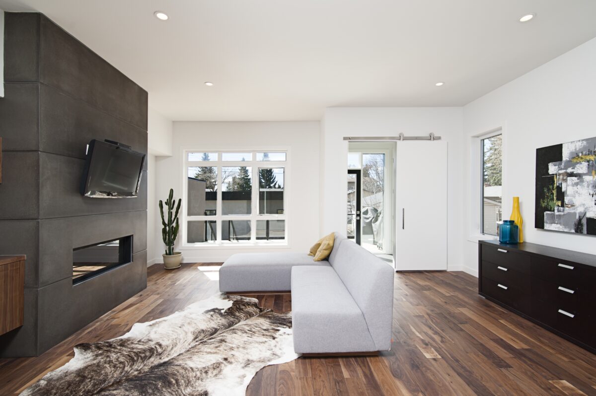 living area with a wall mounted television above a fireplace on a black wall. Dark wooden flooring
