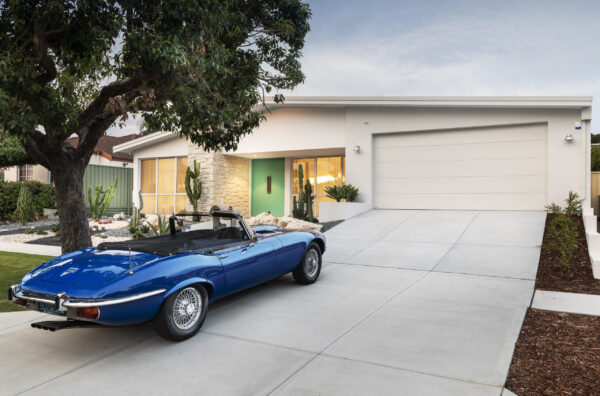 Classic blue convertible parked on the driveway of a single storey home with a green front door