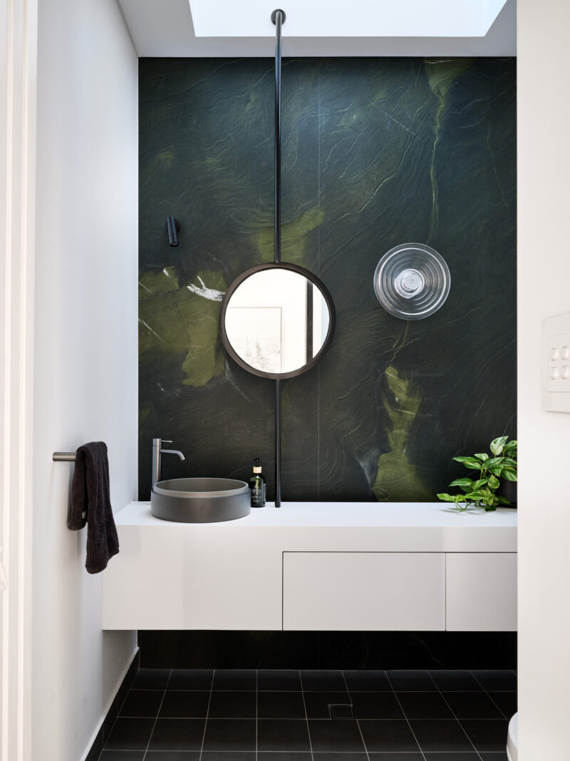 Bathroom with dark green stone feature wall, round mirror and floating vanity