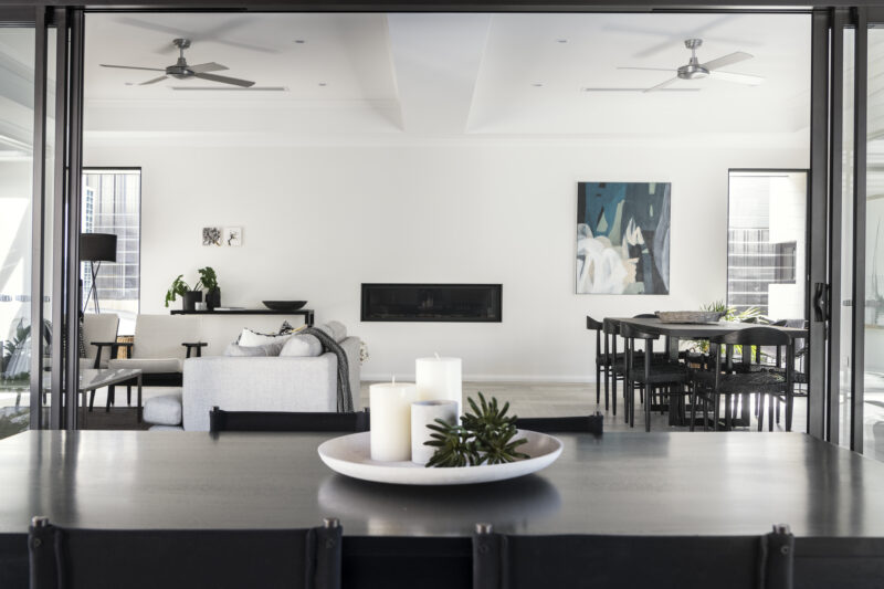 View from the dining table to the living area featuring luxury furnishings, and dark accents for a contemporary feel. This contemporary custom home built by Oswald Homes.