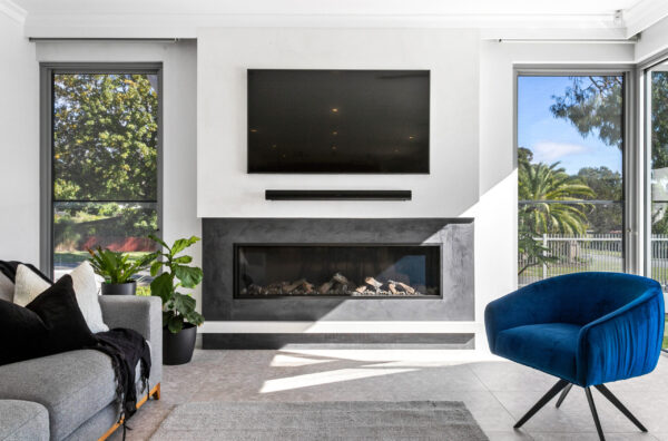 Oswald Homes luxury home design in Perth, living room with linear gas fireplace, stone hearth and blue velvet armchair